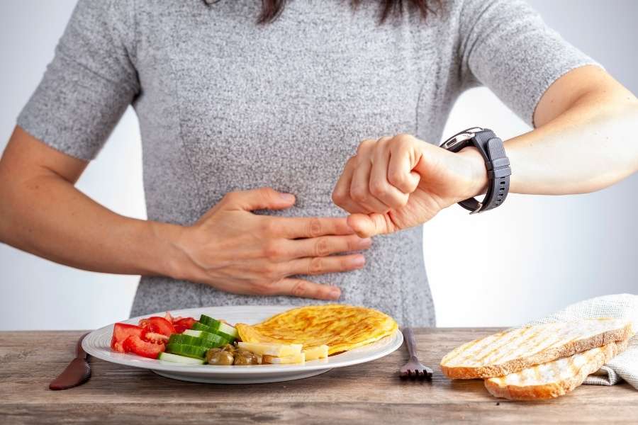 Une femme assise sur un canapé, blottie sous une couverture épaisse, utilise un mouchoir pour se moucher. Ce moment de repos illustre parfaitement les mesures essentielles pour soigner un rhume efficacement chez soi. Le calme et la chaleur aident grandement l'organisme à récupérer de la fatigue.